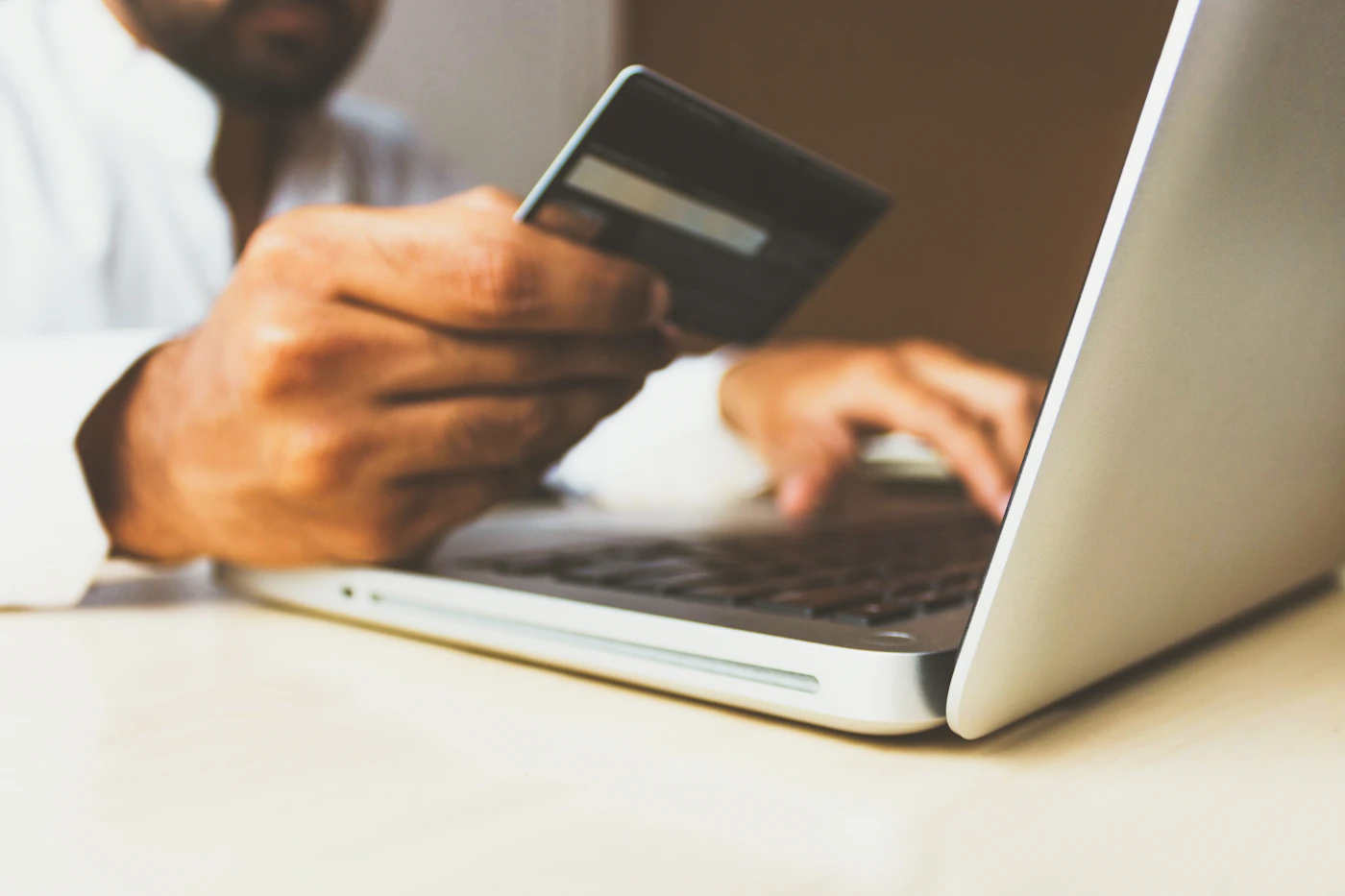 A hand holding a credit card above a receipt and a pen on a desk